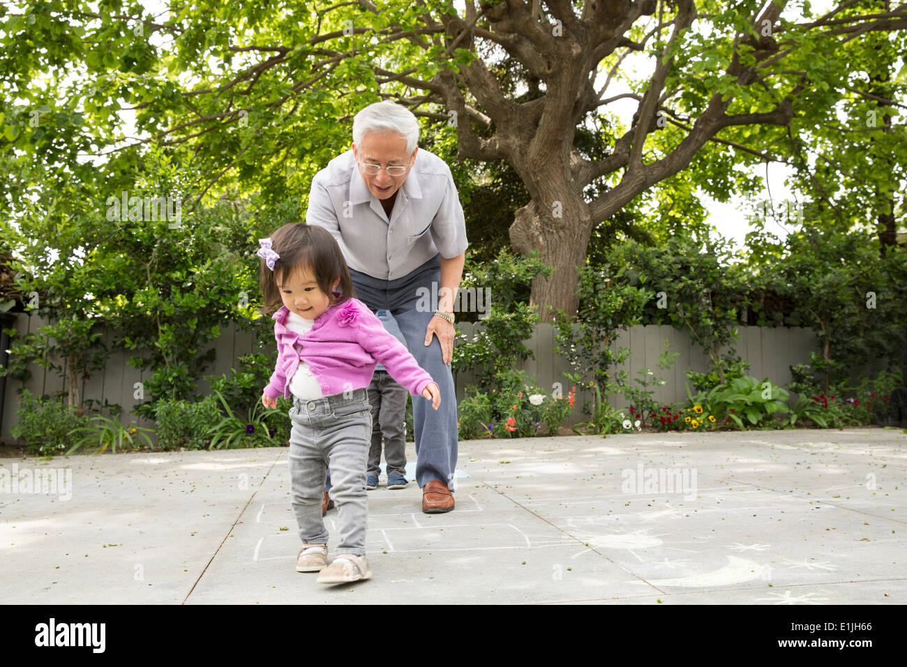 Grandfather playing hopscotch with toddler granddaughter Stock Photo
