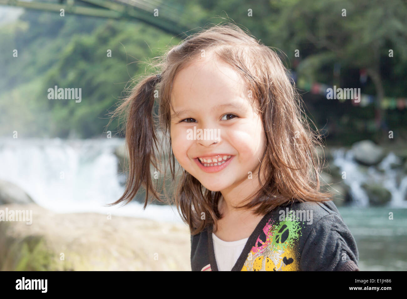 Child standing near a lake with waterfall in background Stock Photo