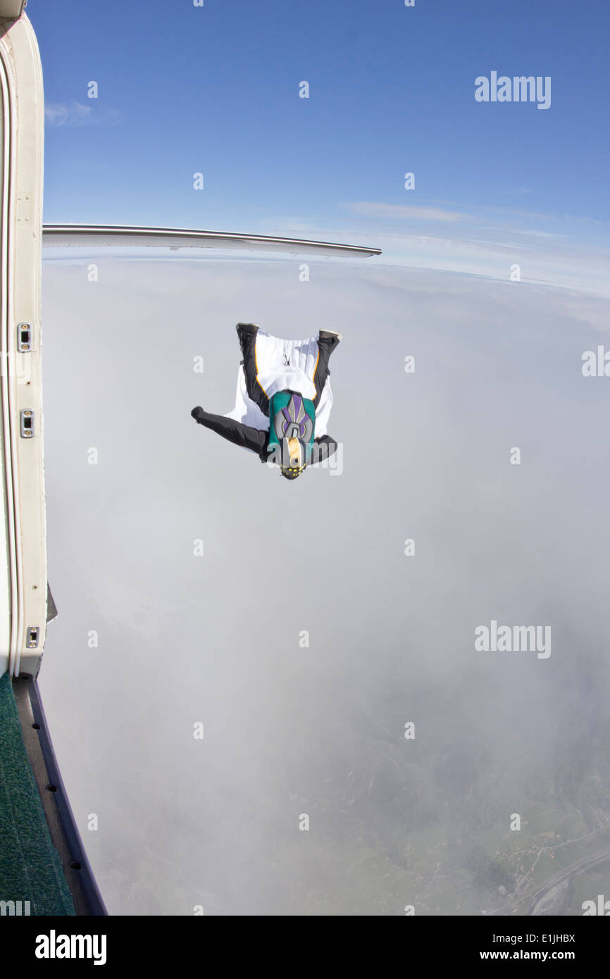 Mid adult man flying above clouds in wingsuit Stock Photo