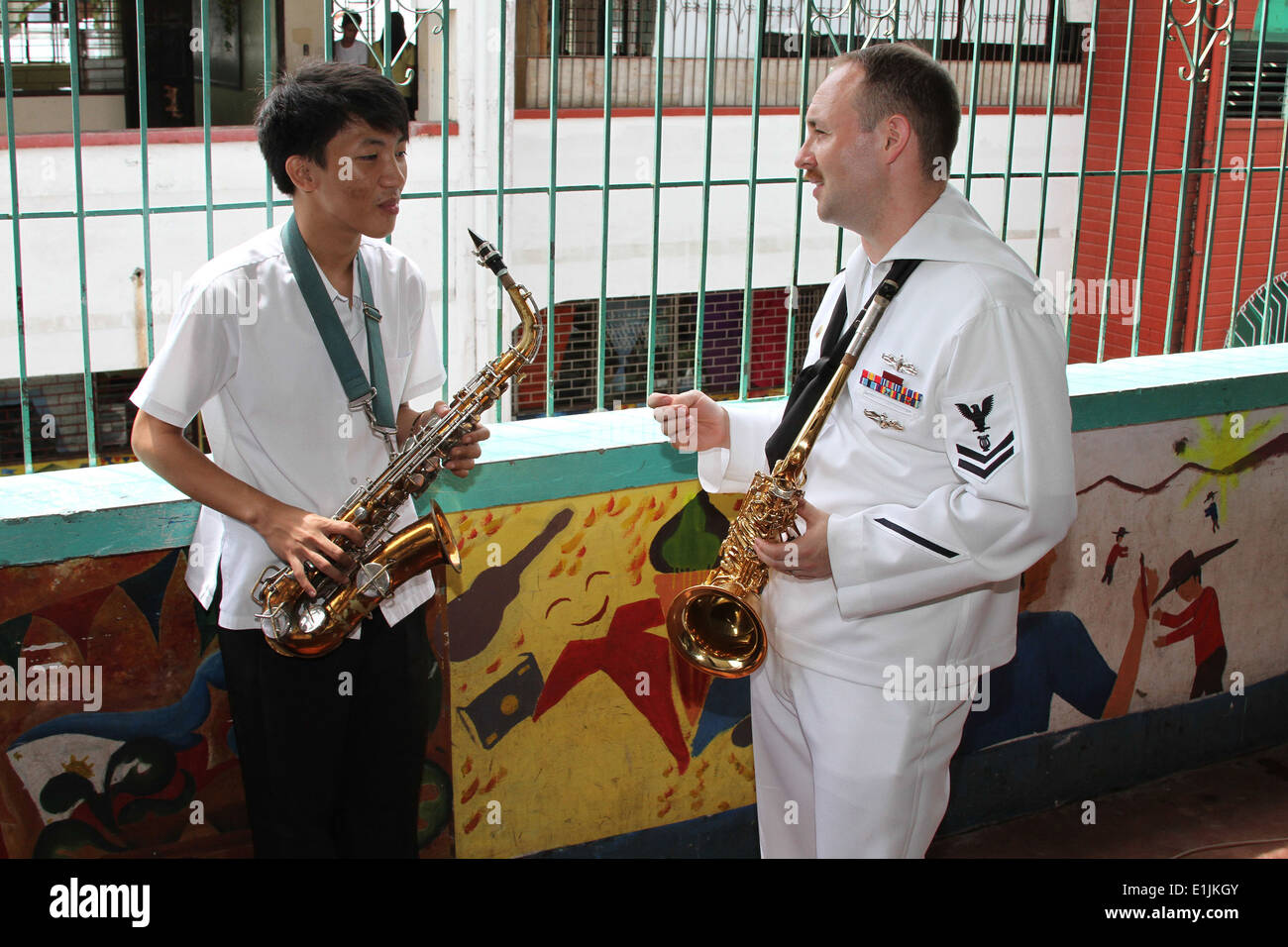 A U.S. Sailor, right, with the U.S. 7th Fleet Band ensemble Orient Express explains breathing techniques for playing the saxoph Stock Photo