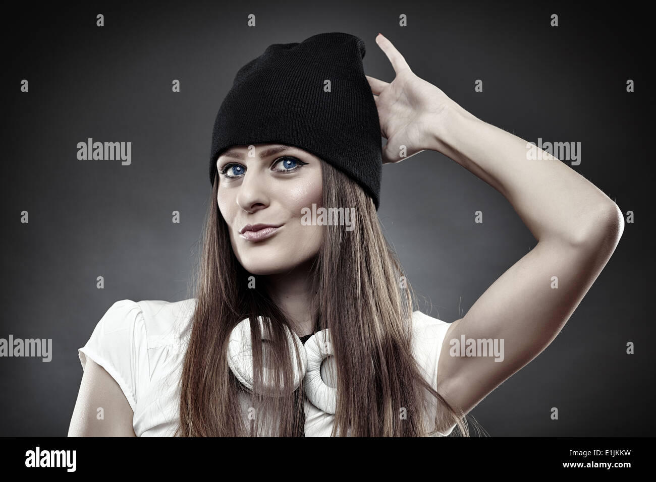 Studio shot of young woman wearing cap and headphones over the neck on gray background Stock