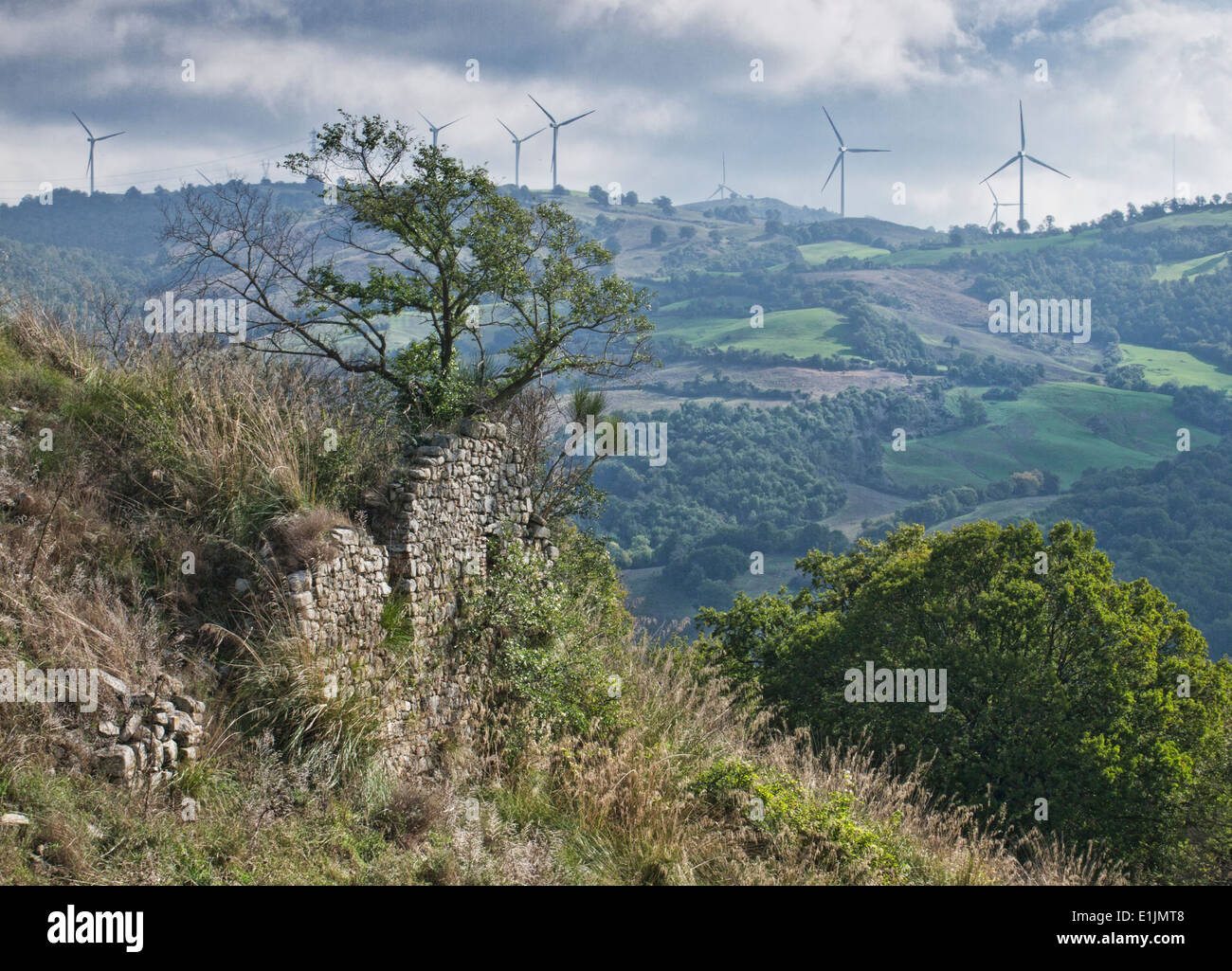 Ruins of the Castello di Cotone, a medieval settlement in Scansano near Grosseto. In background wind turbines modify the rural italian landscape. Stock Photo