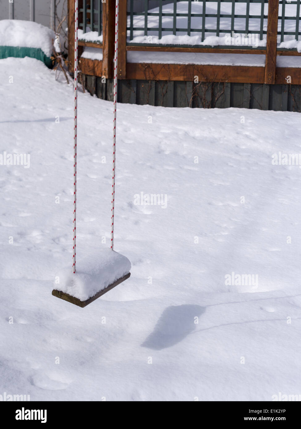Empty Snow Covered Swing. A child's swing piled high with snow hangs in a back yard covered with snow on a sunny day. Stock Photo