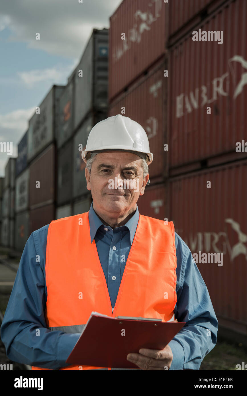 Man with clipboard wearing reflective vest at container port Stock Photo