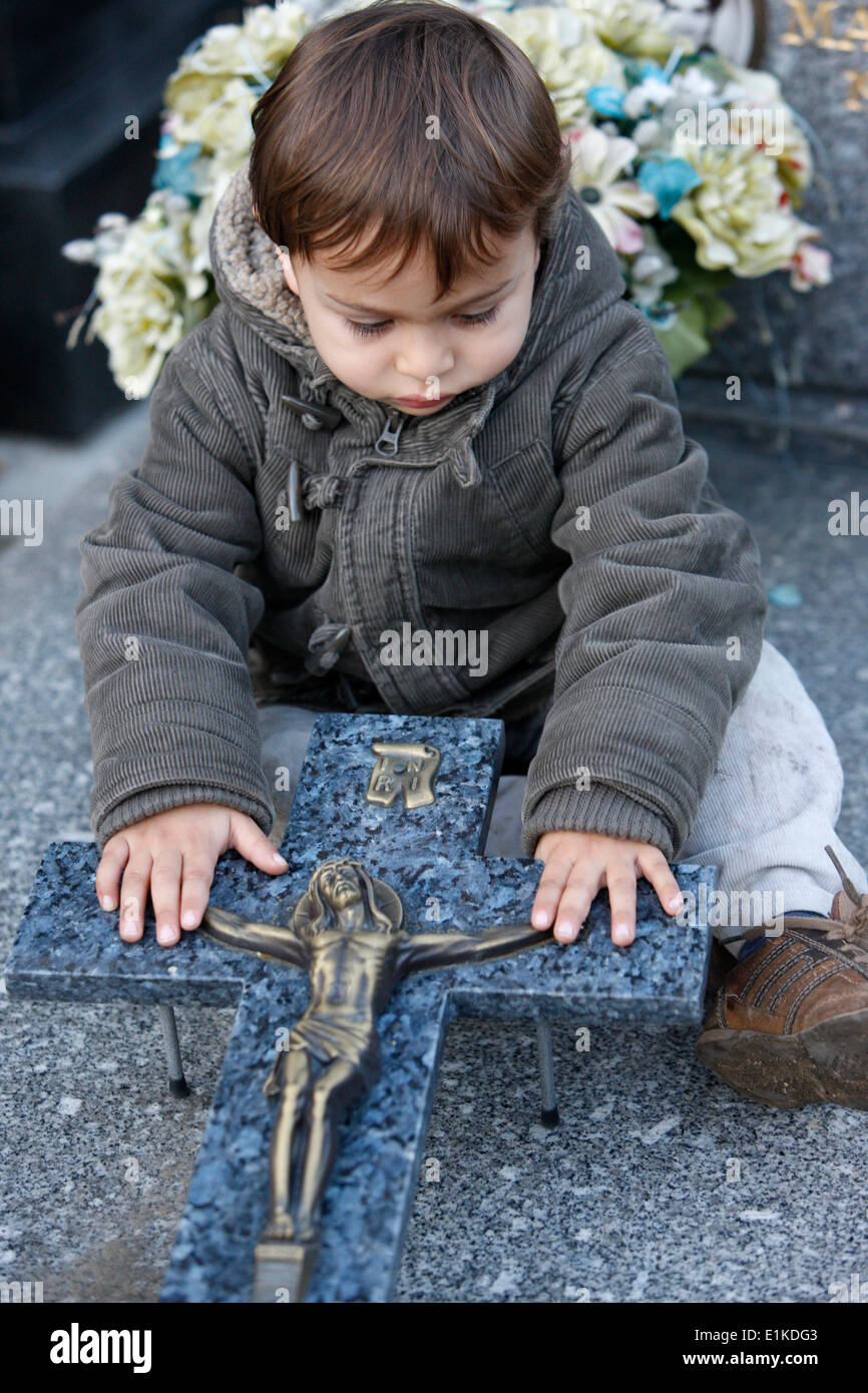 3-year old boy touching a crucifix in a graveyard Stock Photo
