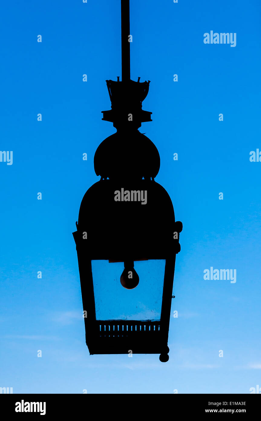 A silhouette of a hanging outdoor light fixture against a blue sky. Stock Photo