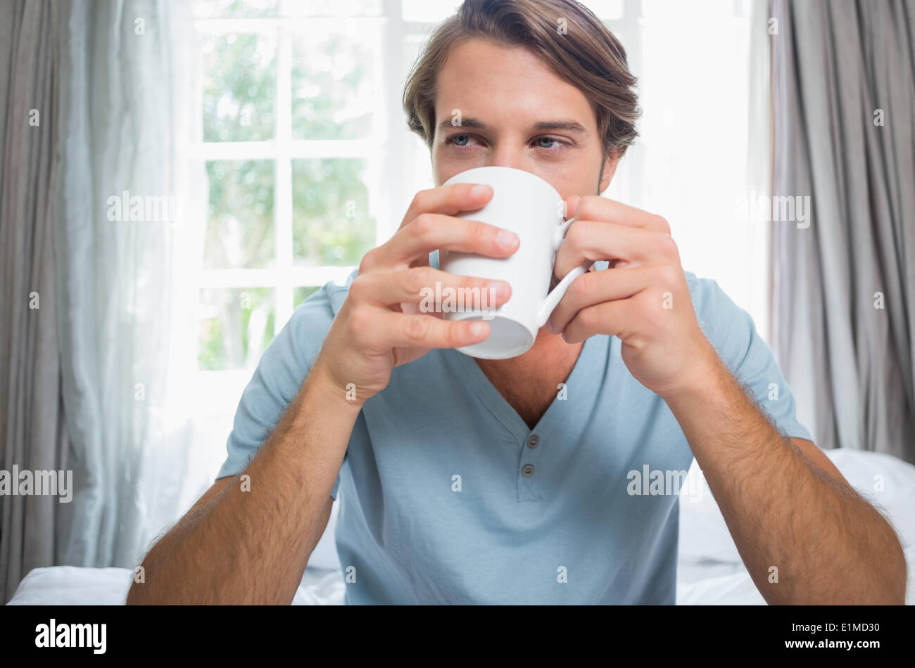 Handsome man sitting on bed drinking coffee Stock Photo