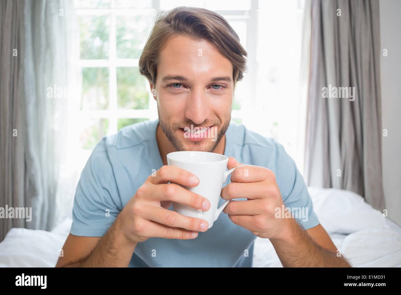 Handsome man sitting on bed drinking coffee Stock Photo