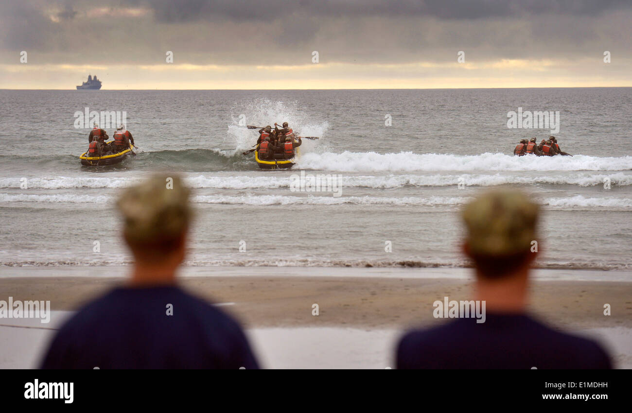 U.S. Navy SEAL candidates paddle inflatable boats into the surf as their instructors