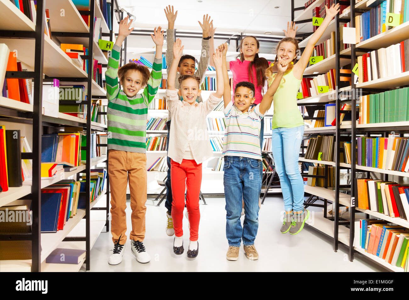 Happy kids jumping with hands up in the library Stock Photo