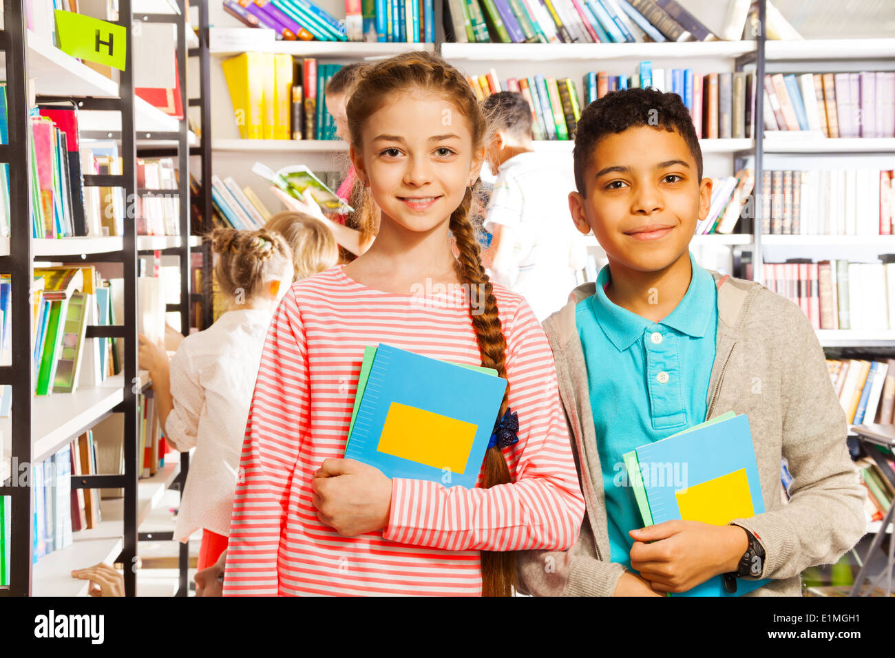 Girl and boy with books standing in library Stock Photo