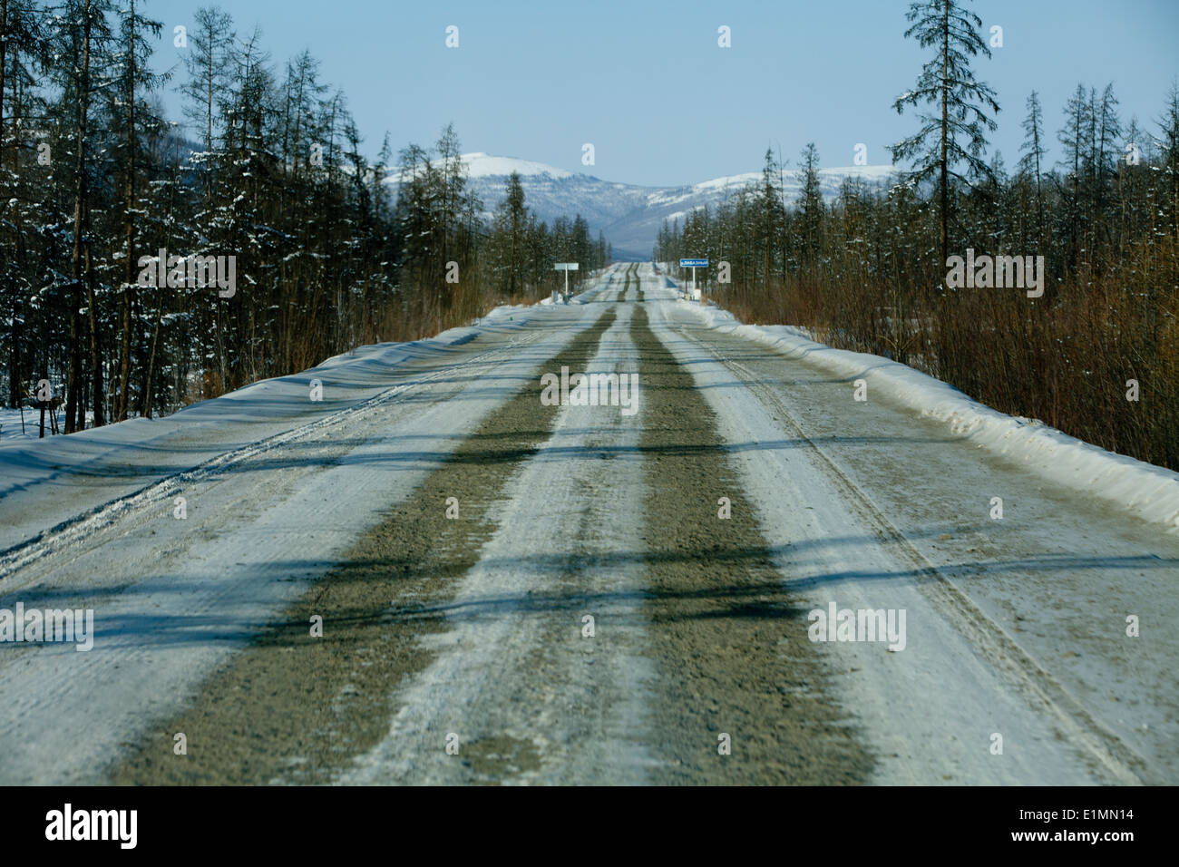 snowy mountains long straight road shadows trees Stock Photo