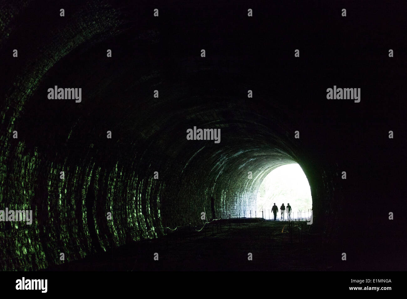 Three women walking out of a dark and gloomy tunnel into the light in Belgium Stock Photo