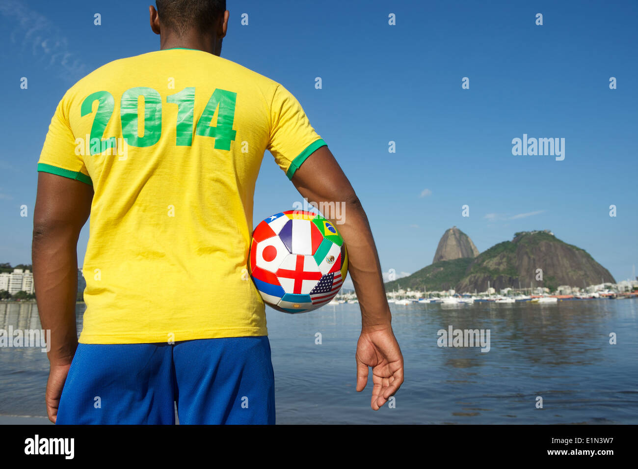 Brazilian football player in 2014 shirt standing with international country flag soccer ball in front of Sugarloaf Pao de Acucar Stock Photo
