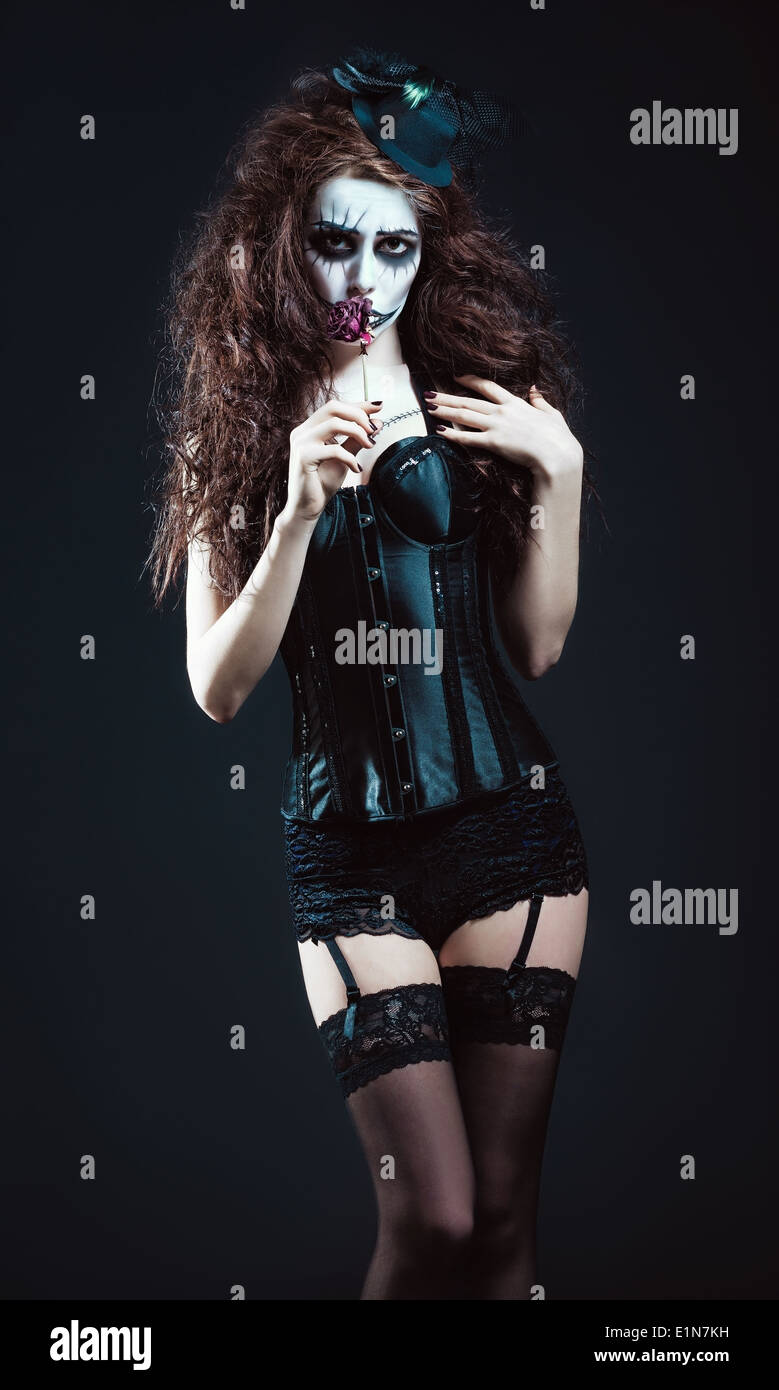 Young woman in the image of a sad gothic freak clown smelling withered flower Stock Photo