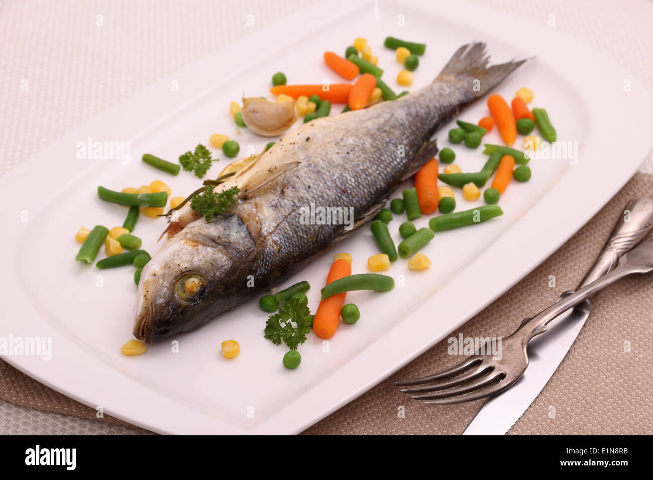 Fried whole sea bass with vegetables and lemon, close up Stock Photo