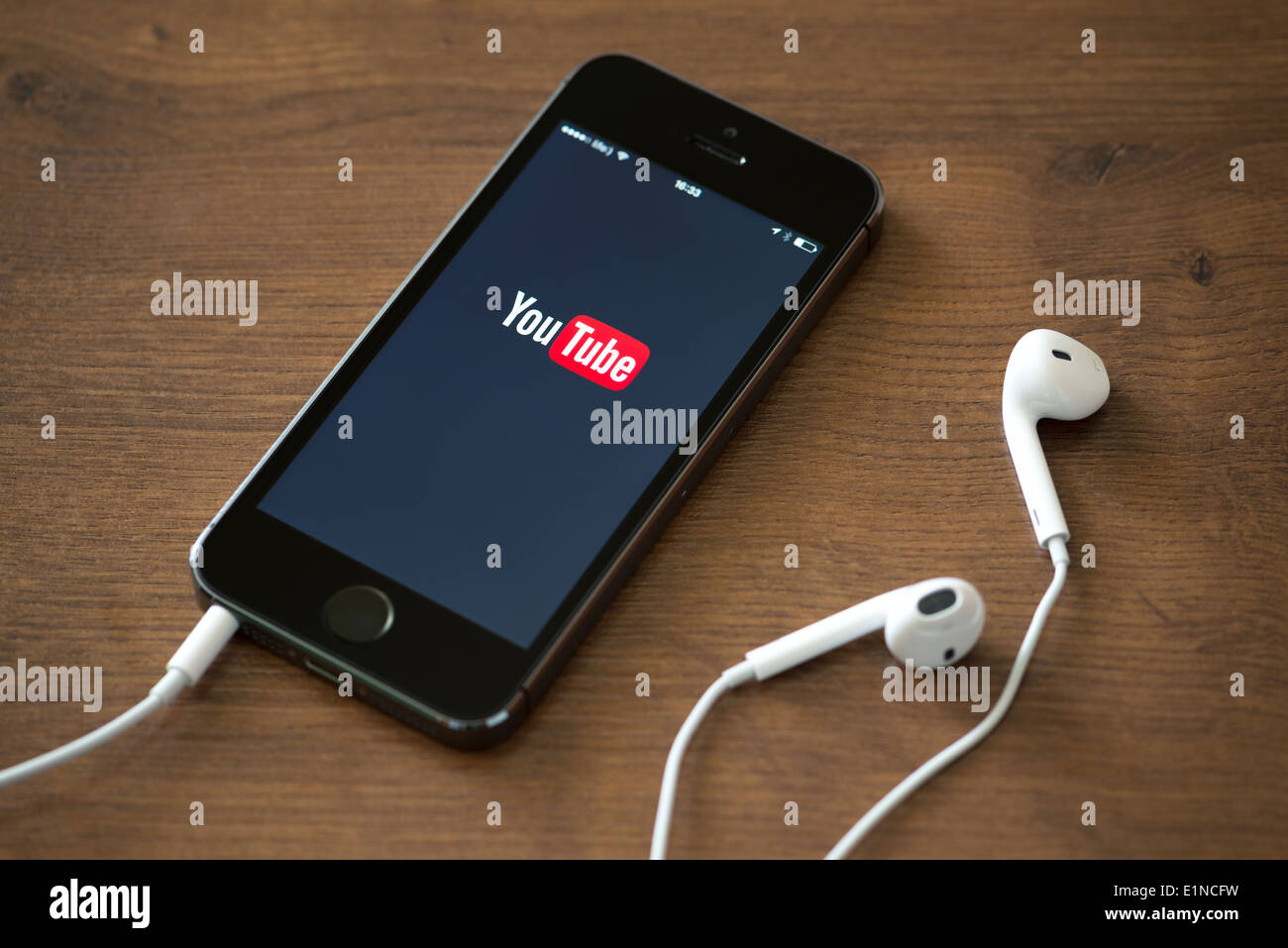 Brand new Apple iPhone 5S with YouTube application service on the screen lying on a desk with headphones. Stock Photo