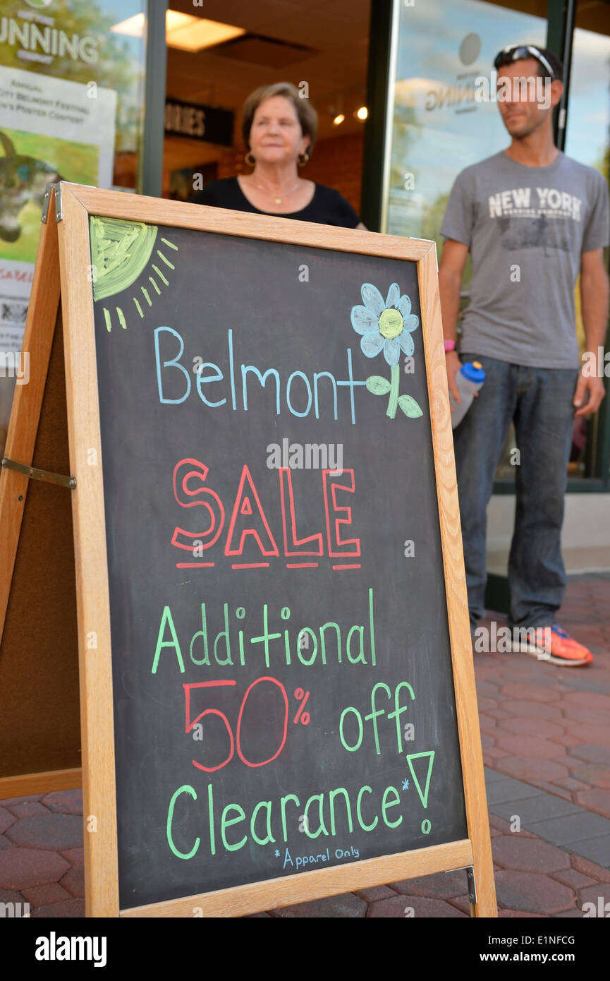 Garden City, New York, U.S. - June 6, 2014 -  ANTHONY RANDOLPHI of Valley Stream, on staff at New York Running Co, is by a chalkboard easel sign announcing the store's Belmont Sale, during the 17th Annual Garden City Belmont Stakes Festival, celebrating the 146th running of Belmont Stakes at nearby Elmont the next day. There was street festival family fun with live bands, food, pony rides and more, and a main sponsor of this Long Island night event was The New York Racing Association Inc. Stock Photo
