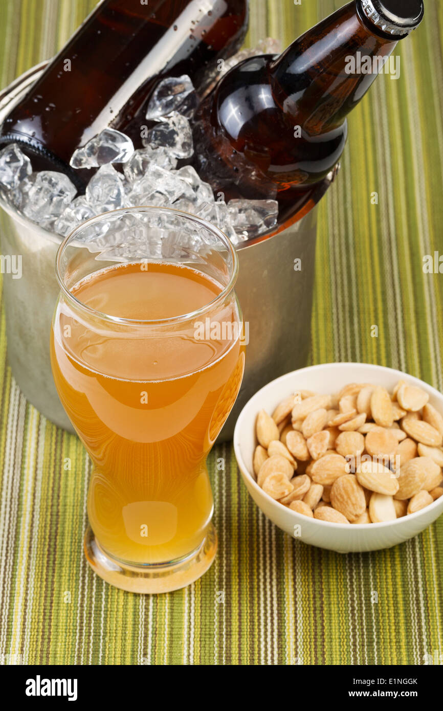 Closeup vertical photo of a golden beer in tall glass with salted nuts in small bowl with bottled beer in bucket of ice Stock Photo