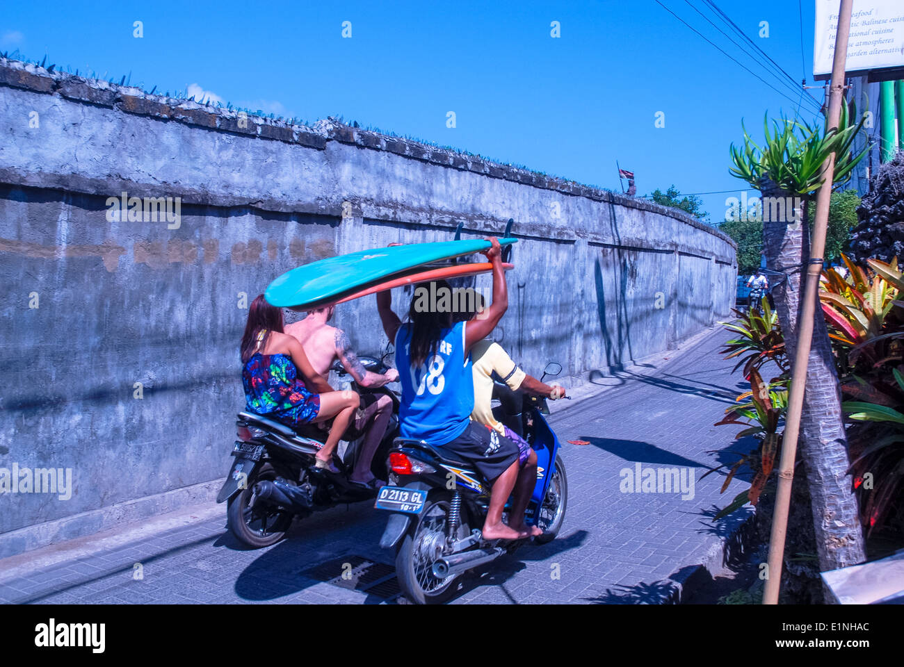 tourists on bikes or scooters with surf oards on their head towards the beach at Kuta, Bali, Indonesia Stock Photo