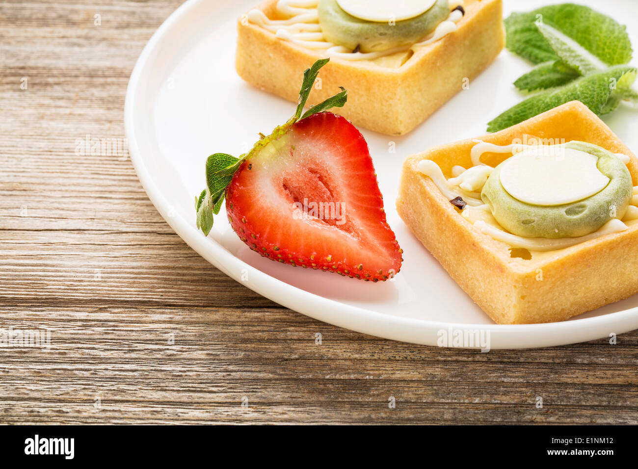 dessert - tarts with strawberry and fresh peppermint on white plate against grained weathered wood, top view Stock Photo