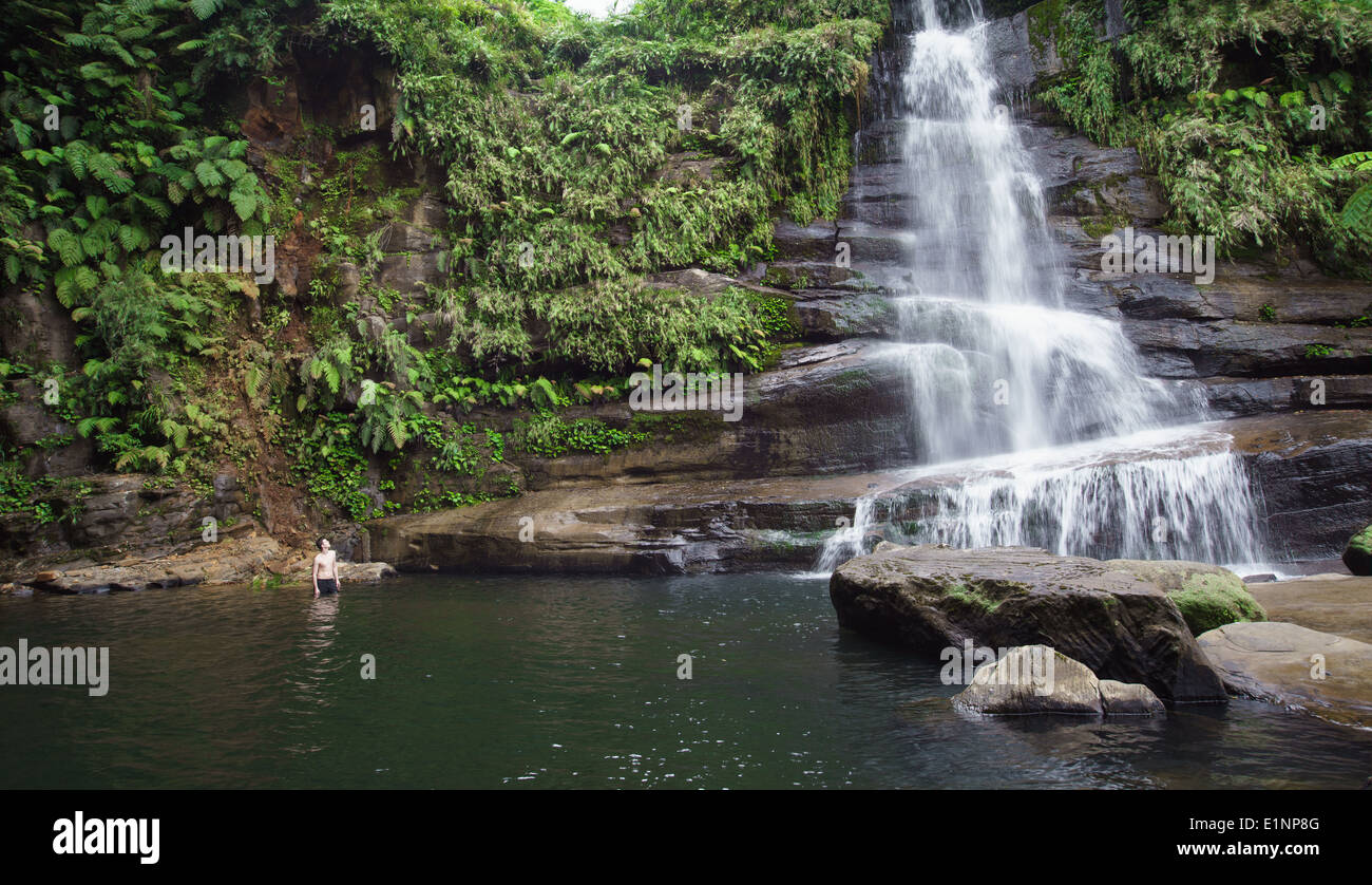 Man at admiring huge Jungle waterfall hidden in lush green rain forest of Iriomote island, Okinawa, tropical Japan Stock Photo