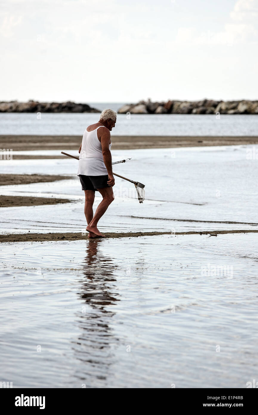 Old man on a beach in Rimini looking for shell fish Stock Photo - Alamy