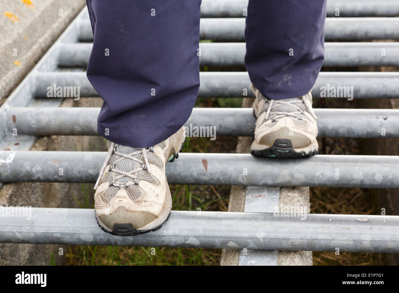 Woman walker wearing walking shoes stepping cautiously and carefully over bars on a cattle grid on a country track. England, UK, Britain. Stock Photo