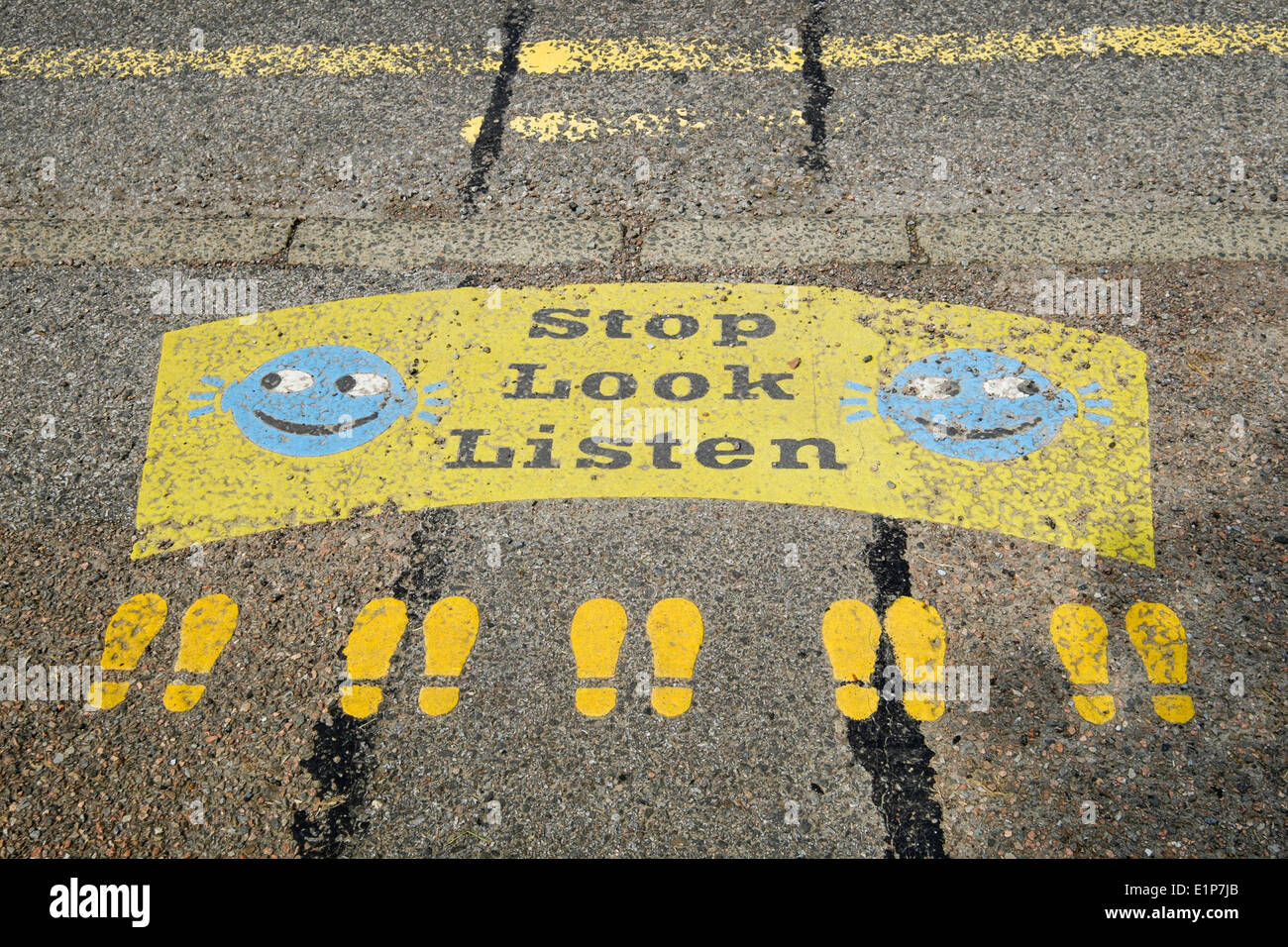 Stop Look Listen sign with smiley faces and footprints painted on a roadside kerb near a primary school road crossing. Scotland UK Britain Stock Photo