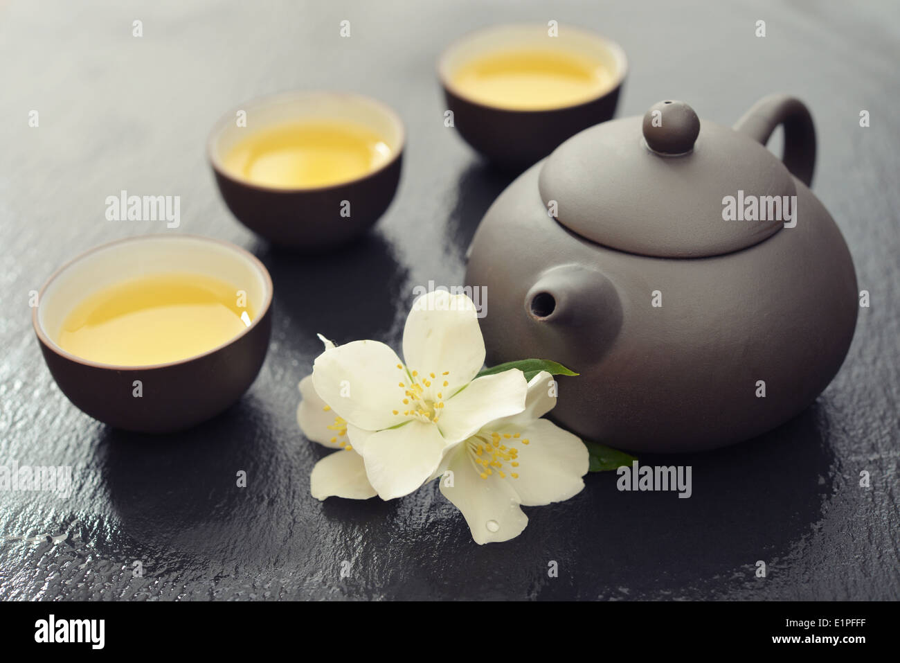 Green tea in cups with jasmine flowers and teapot on wet graphite background Stock Photo