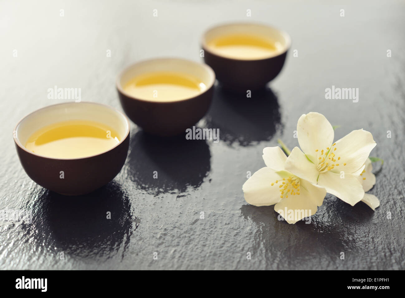 Green tea in cups with jasmine flowers on wet graphite background Stock Photo