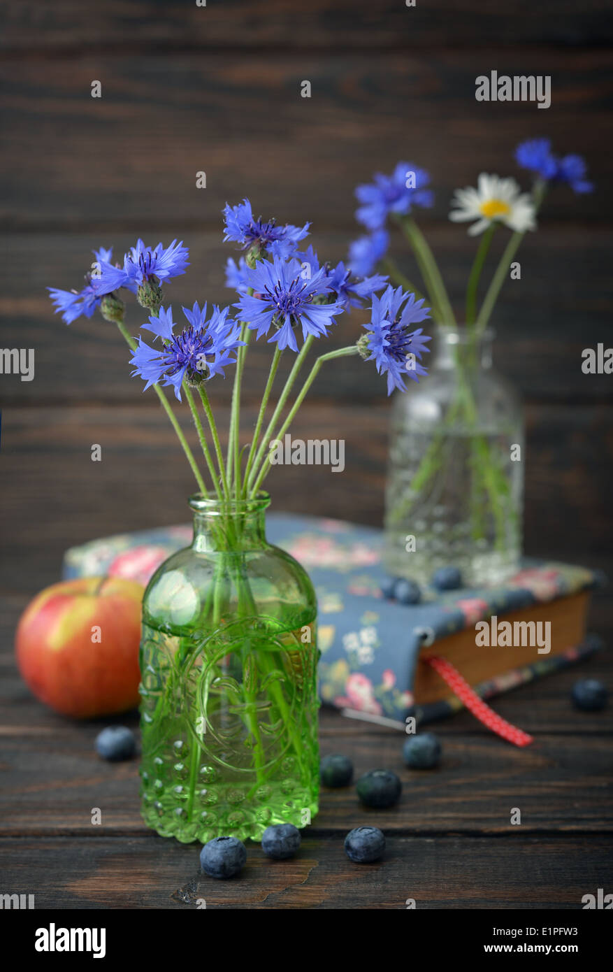 Cornflowers in vintage bottle with berries on wooden background Stock Photo