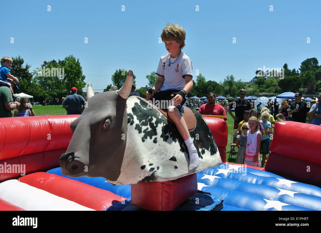 June 8th, 2014 Mill Valley, California. Small boy rides mechanical bull at Strawberry Recreation Center 65th annual festival while parents and visitors cheer him on. Stock Photo