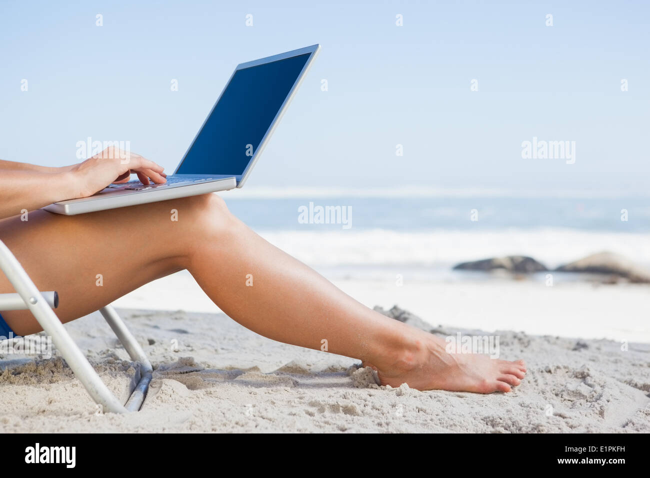 Woman sitting on beach using her laptop Stock Photo