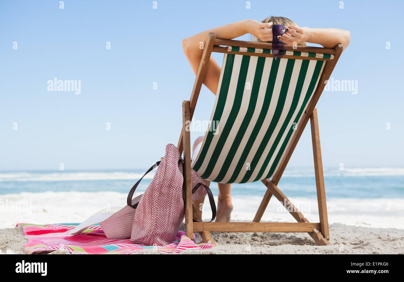 Woman sitting in deck chair at the beach with her beach bag and towel Stock Photo
