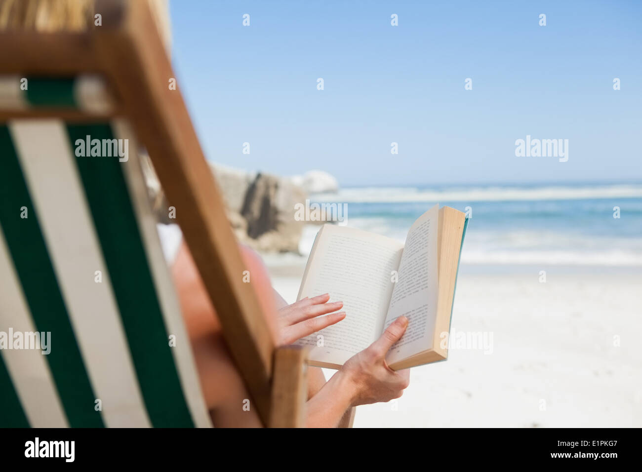 Woman sitting in deck chair at the beach reading Stock Photo