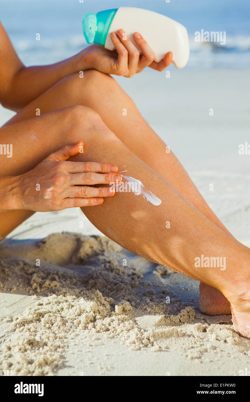 Woman sitting on the beach applying suncream Stock Photo