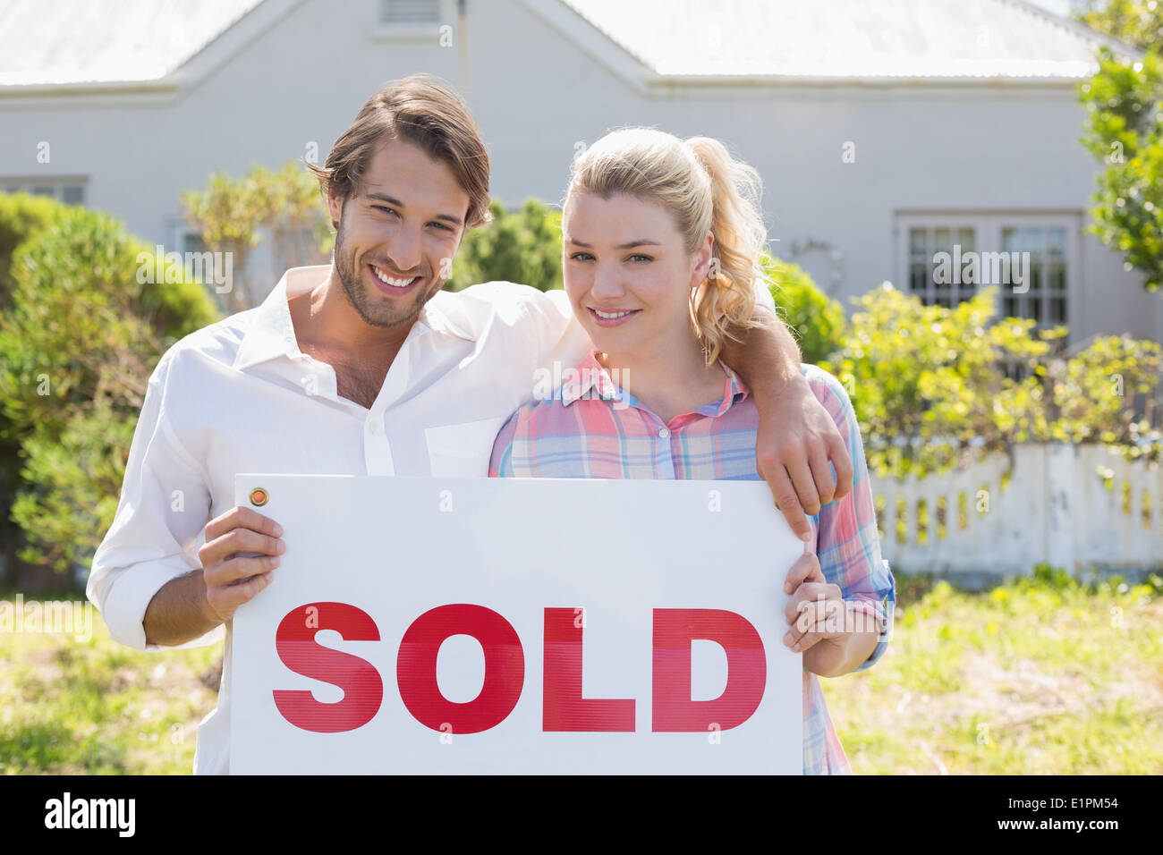 Cute couple standing together in their garden holding sold sign Stock Photo