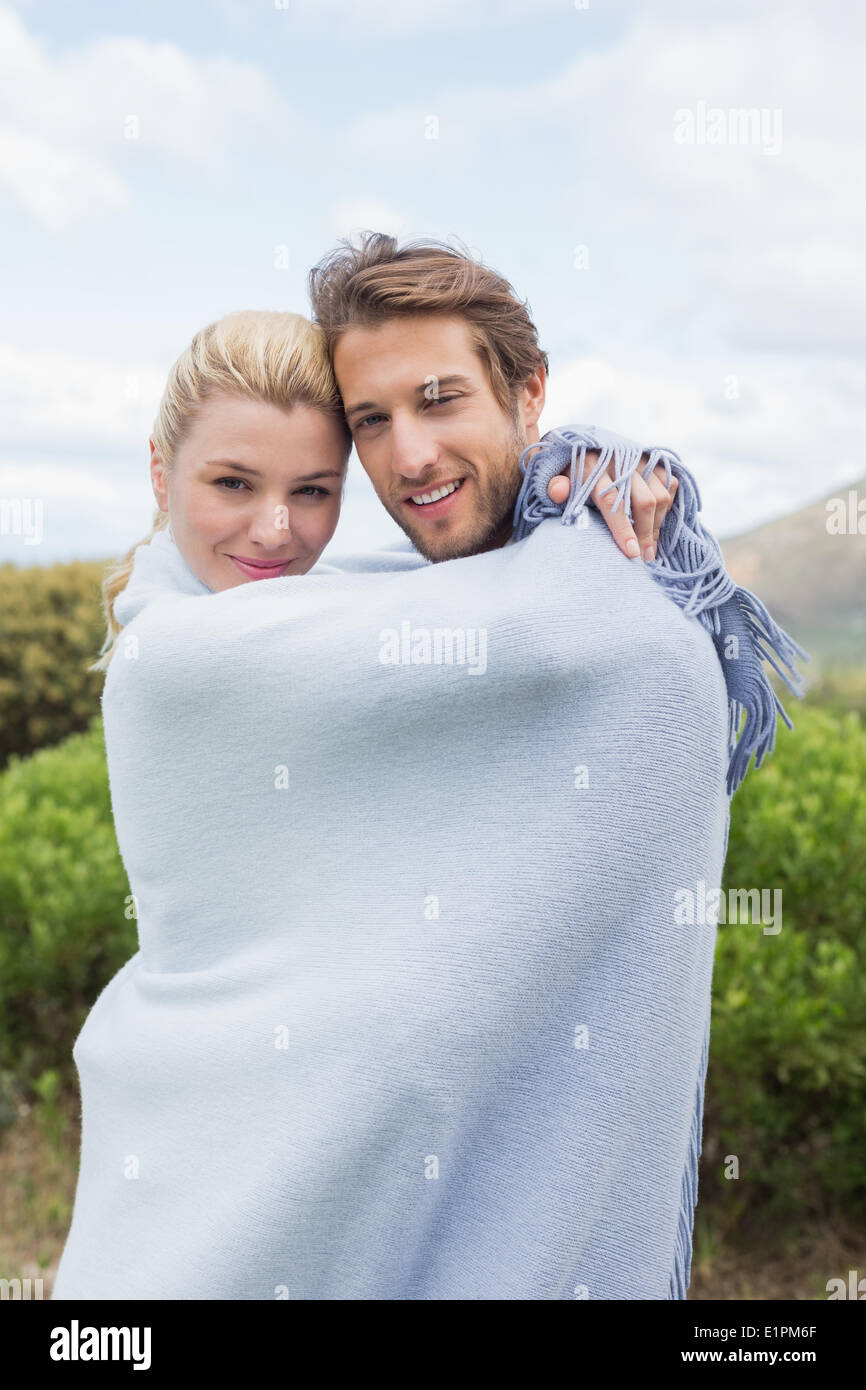 Cute smiling couple standing outside wrapped in blanket Stock Photo