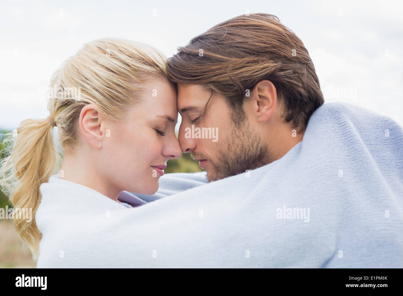 Cute affectionate couple standing outside wrapped in blanket Stock Photo