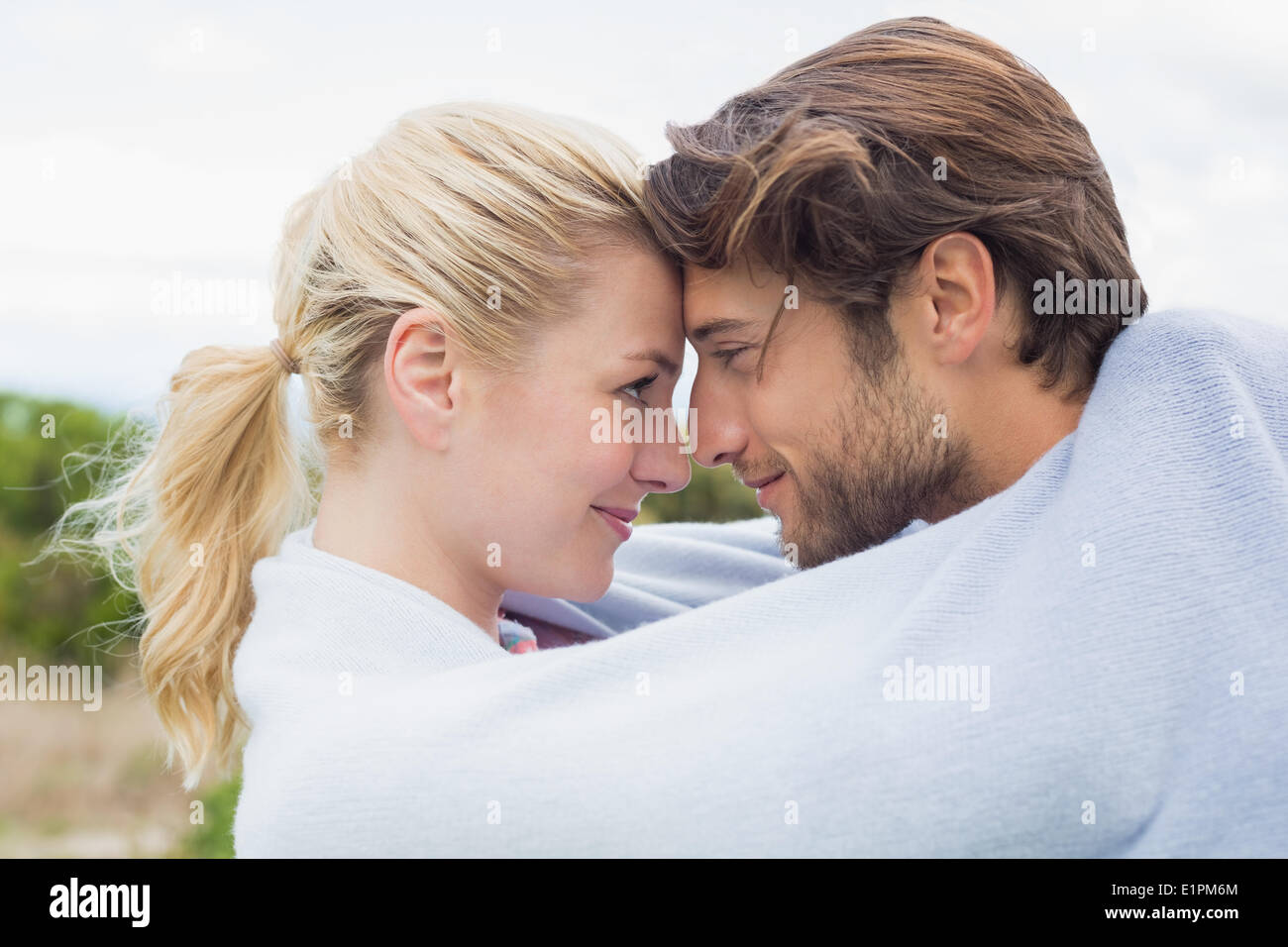 Cute affectionate couple standing outside wrapped in blanket Stock Photo
