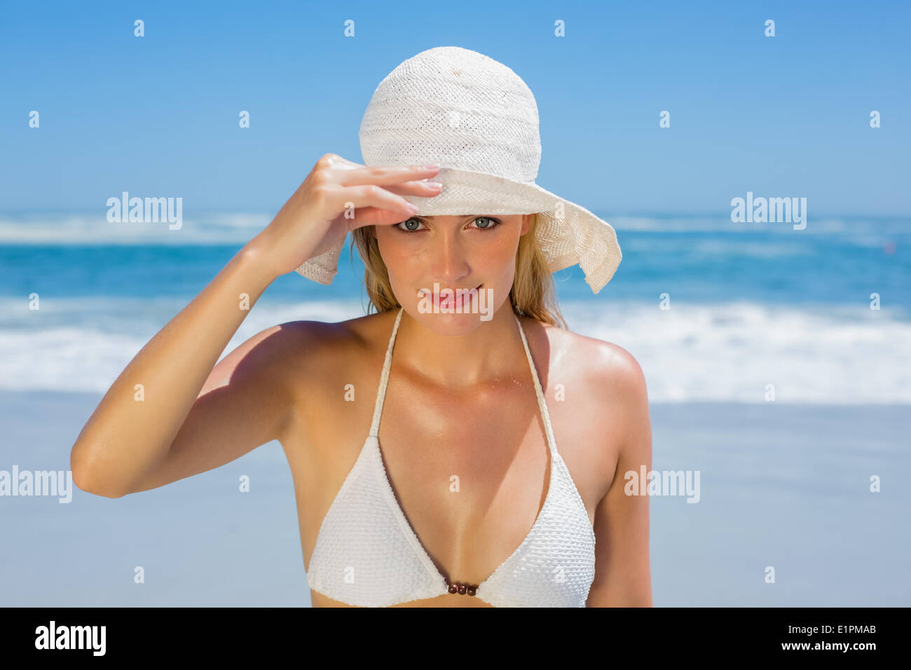 Smiling blonde in white bikini and sunhat on the beach Stock Photo