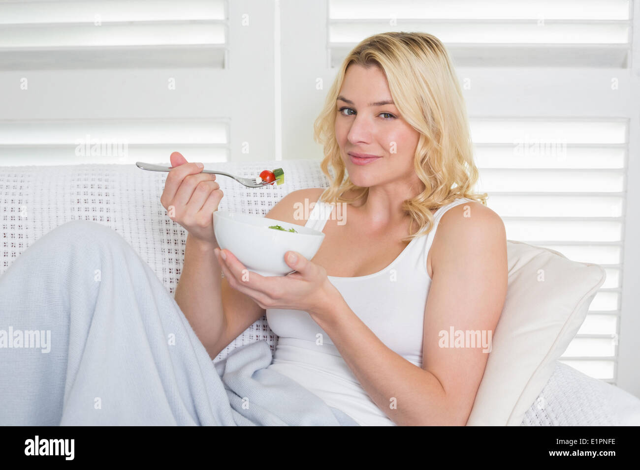 Happy blonde relaxing on the couch eating a salad Stock Photo