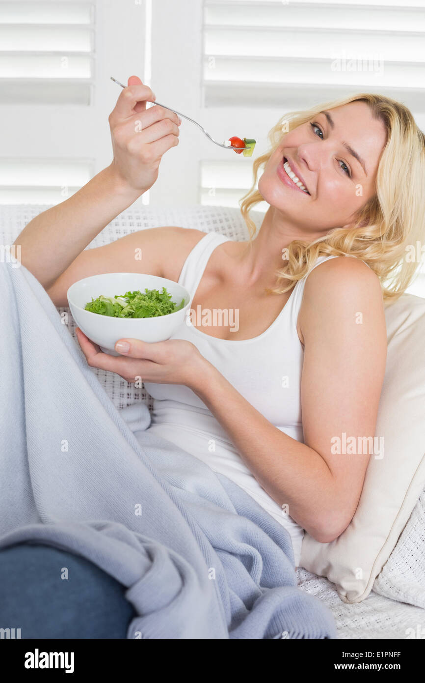 Happy blonde relaxing on the couch eating a salad Stock Photo