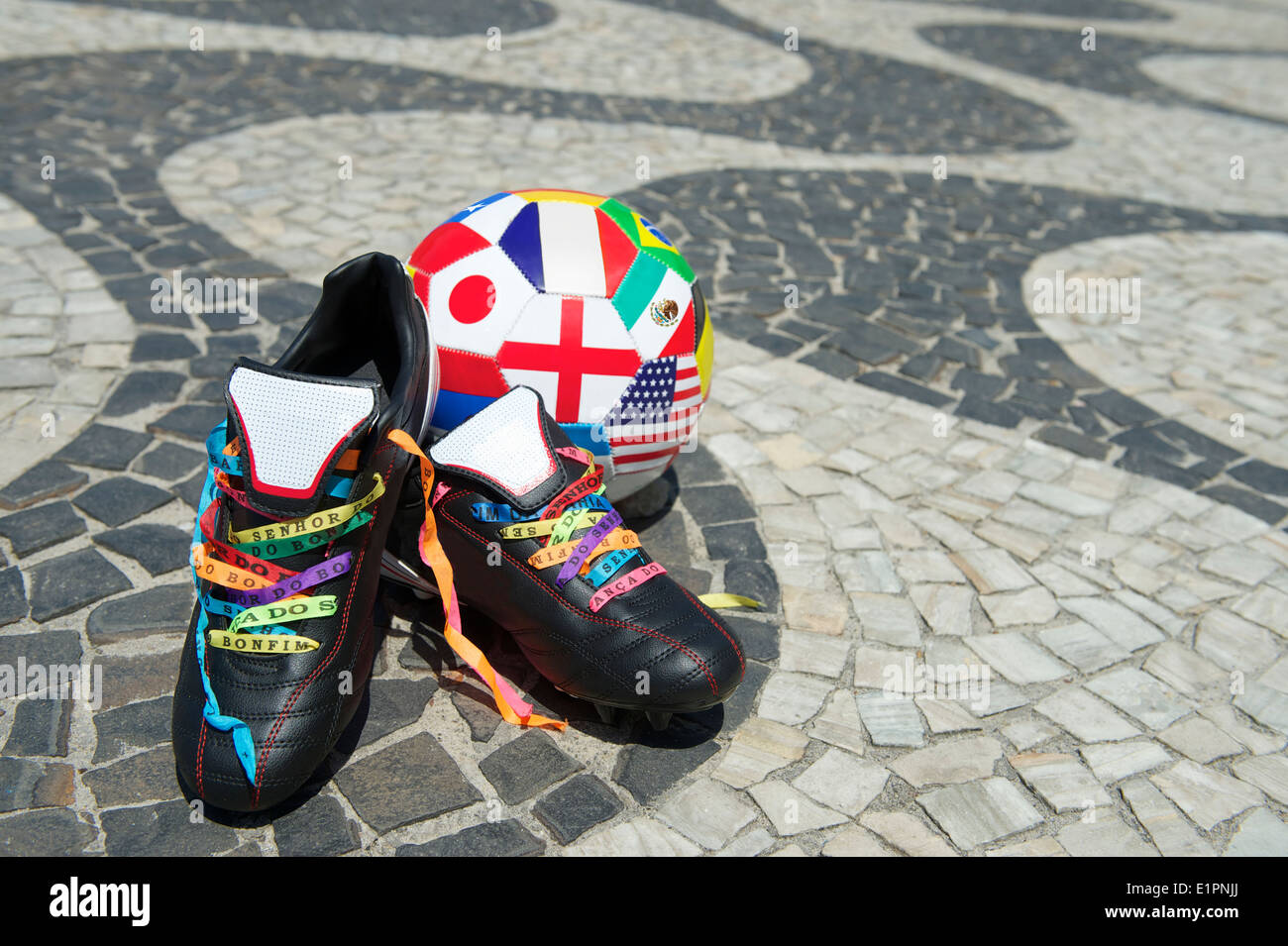 Good luck football boots cleats laced with Brazilian wish ribbons on the Copacabana Beach sidewalk with international flag ball Stock Photo