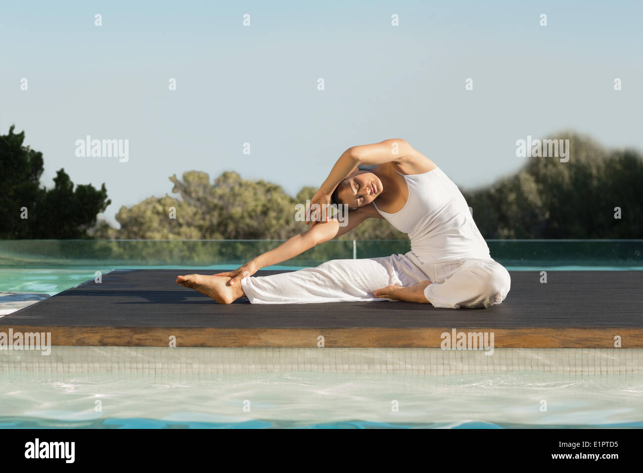Peaceful brunette in janu sirsasana yoga pose poolside Stock Photo