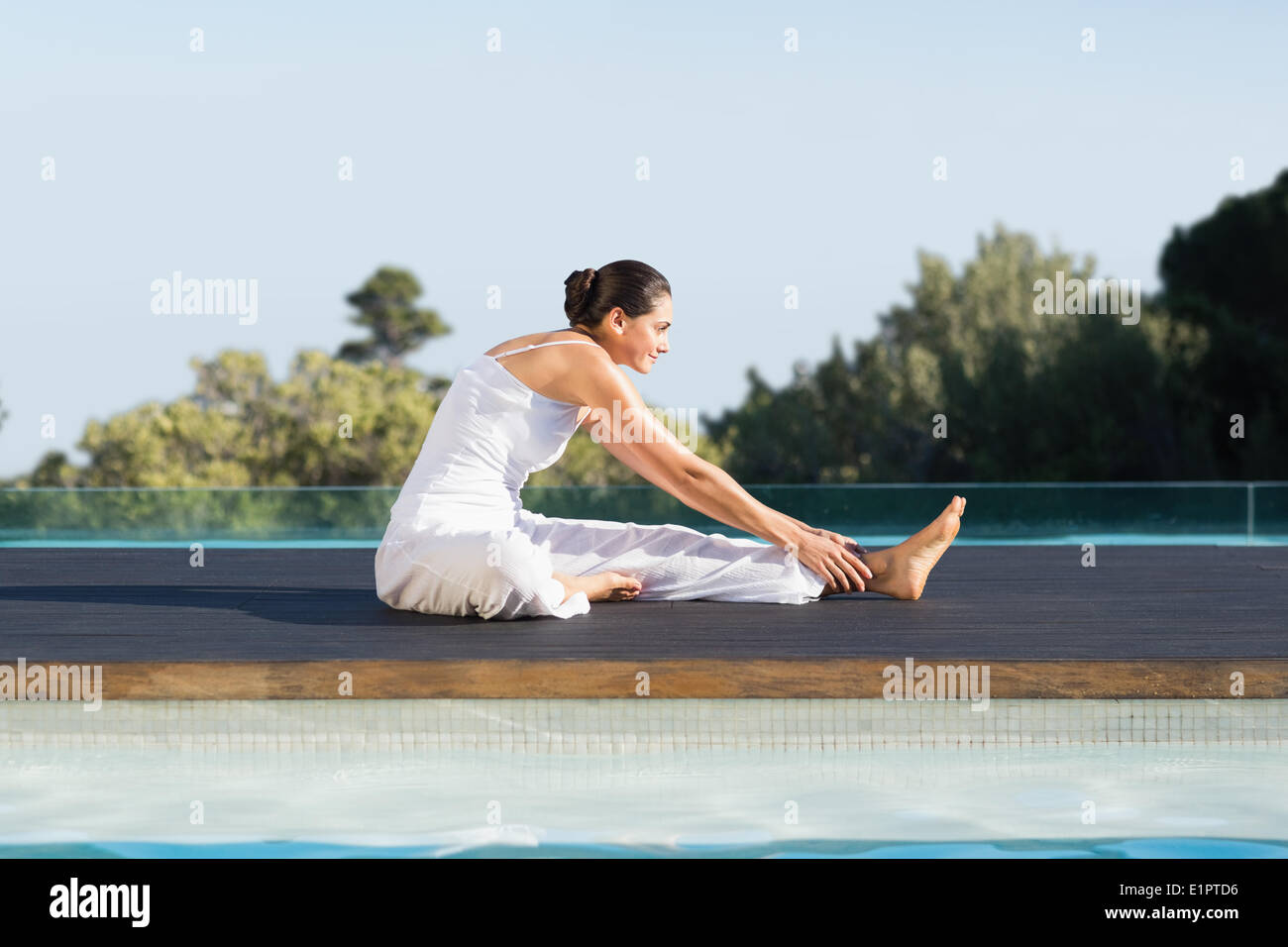 Peaceful brunette in janu sirsasana yoga pose poolside Stock Photo
