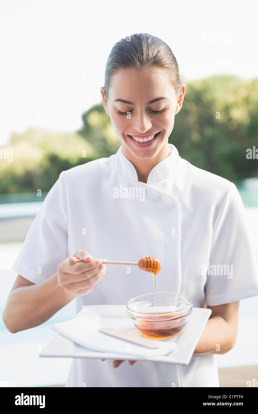 Smiling beauty therapist holding plate with honey Stock Photo