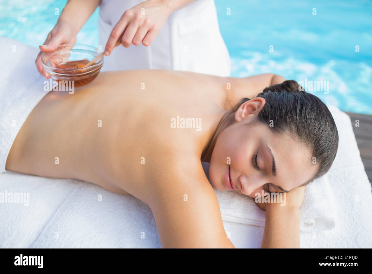 Smiling brunette getting a honey beauty treatment poolside Stock Photo