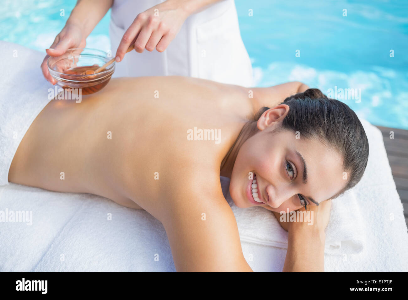 Smiling brunette getting a honey beauty treatment poolside Stock Photo